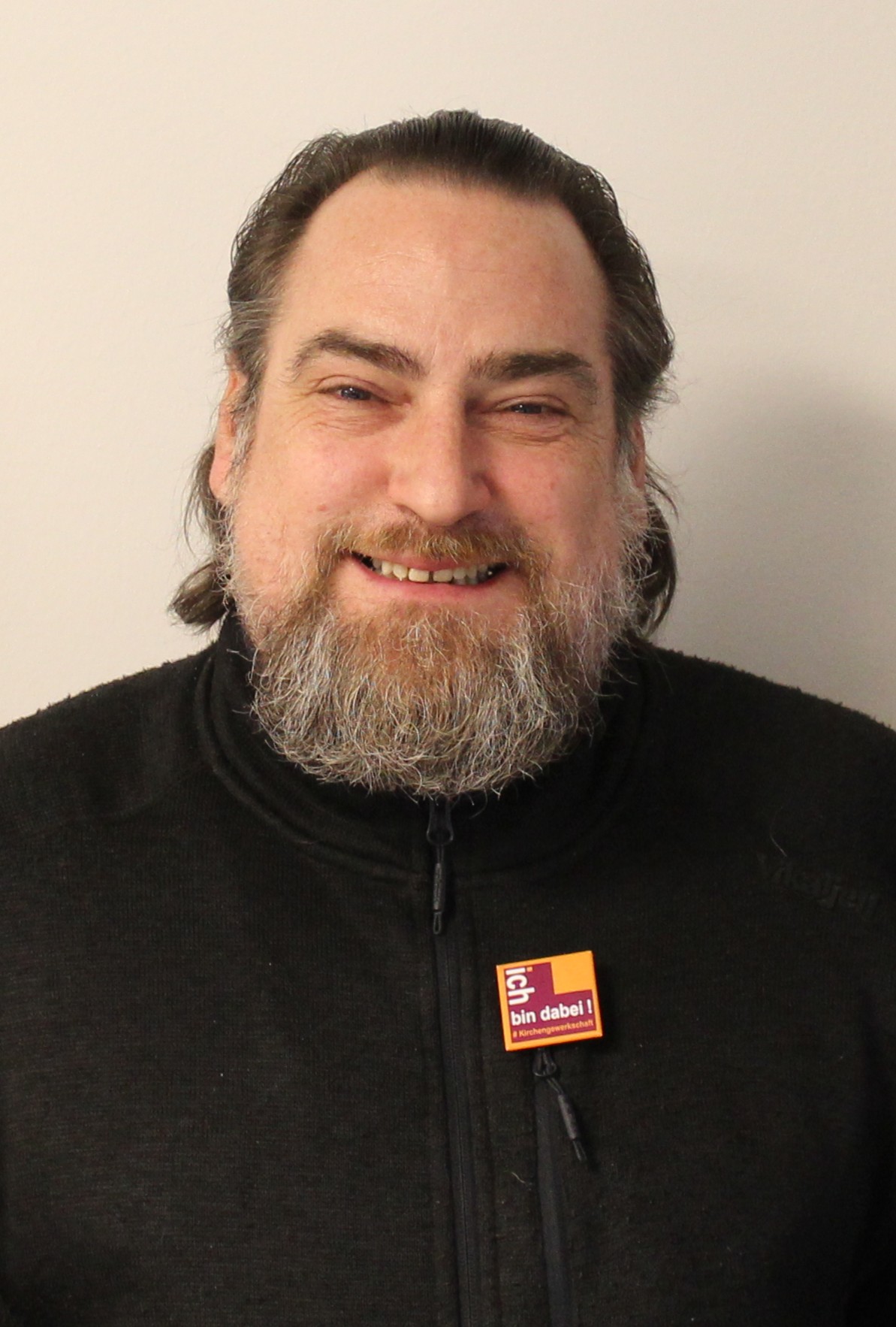 Freundlicher Mann mit Bart trägt "bin dabei!" Button. Kirchengewerkschaft Hessen.