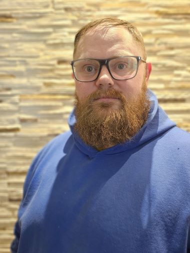 Mann mit Bart, Brille und blauem Hoodie vor Steinwand. Porträt eines Mannes mit Bart.