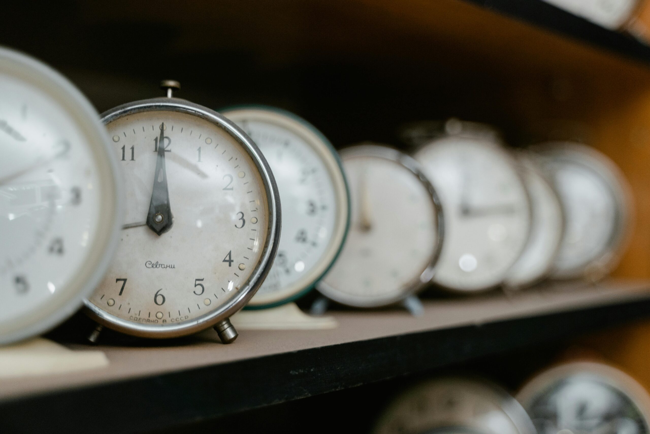 A collection of vintage analogue alarm clocks arranged on a wooden shelf.