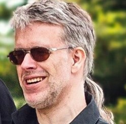 Mann mit Sonnenbrille und Pferdeschwanz lächelt