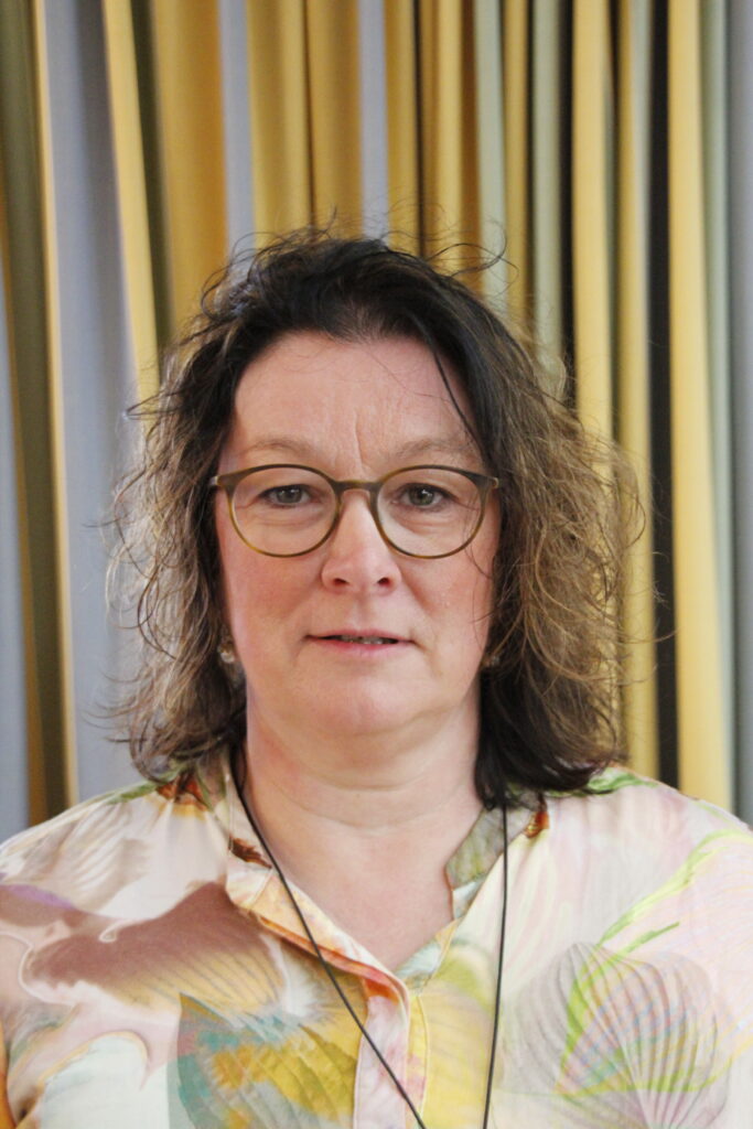 Porträt einer Frau mit Brille, im Hintergrund bunte Streifen
