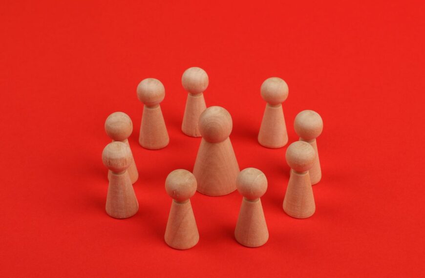 Wooden figurines arranged in a circle on a vibrant red backdrop, creating a crafted minimalist still life.