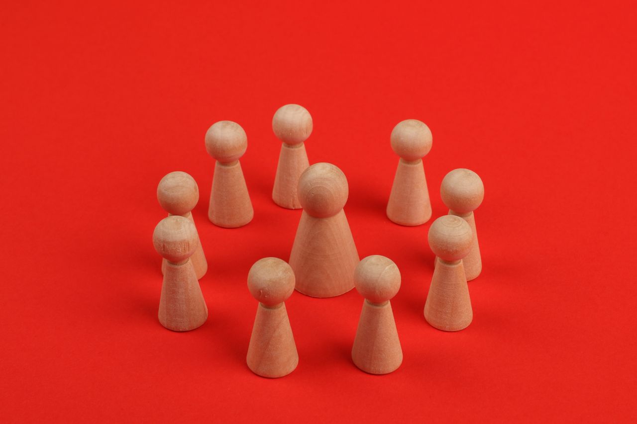 Wooden figurines arranged in a circle on a vibrant red backdrop, creating a crafted minimalist still life.